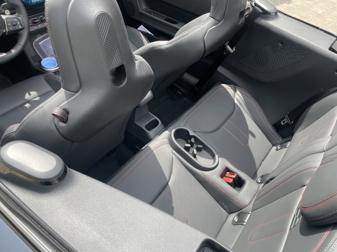 Mini Cooper C Cabrio hinten sitzen auf den hinteren zwei Sitzplätzen, dazwischen ein Becher Anhalter