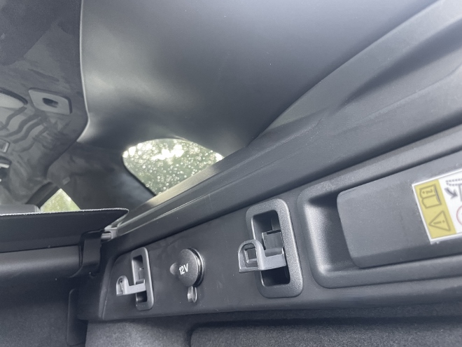 Range Rover Velar P400 AWD Test: Kleiderhaken und Hängehaken und eine 12 V Steckdose und der Schalter für das flach legen der Sitzbank seitlich im Kofferraum